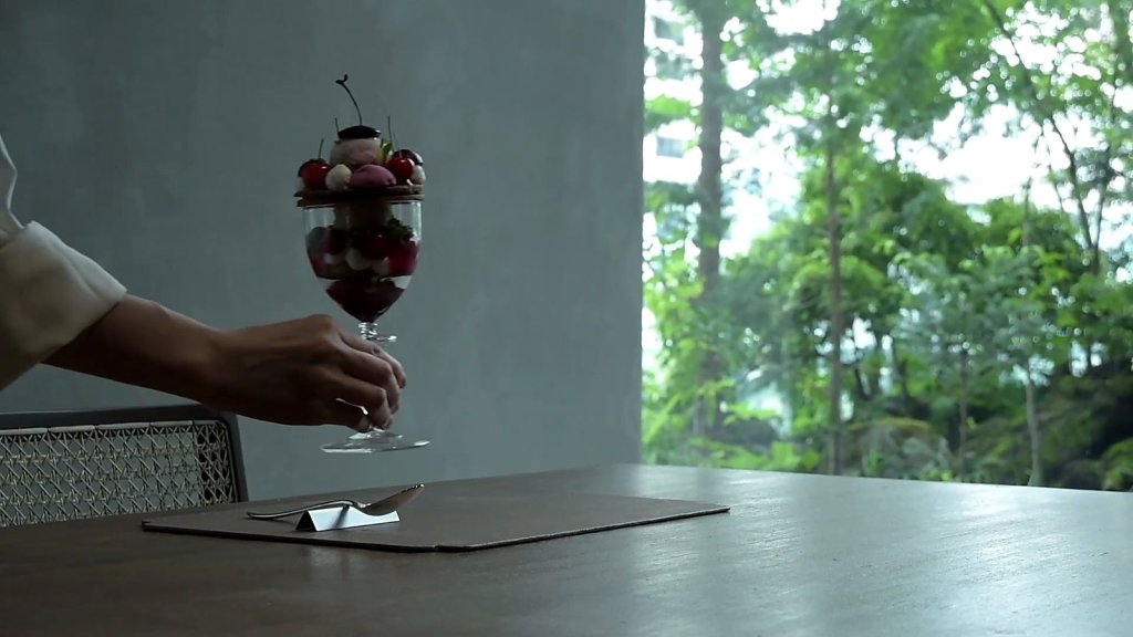 Hand placing a cherry parfait by a window full of forest