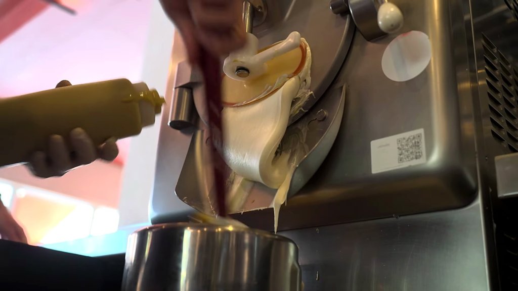 Gelato extruding from a batch freezer into a steel tub
